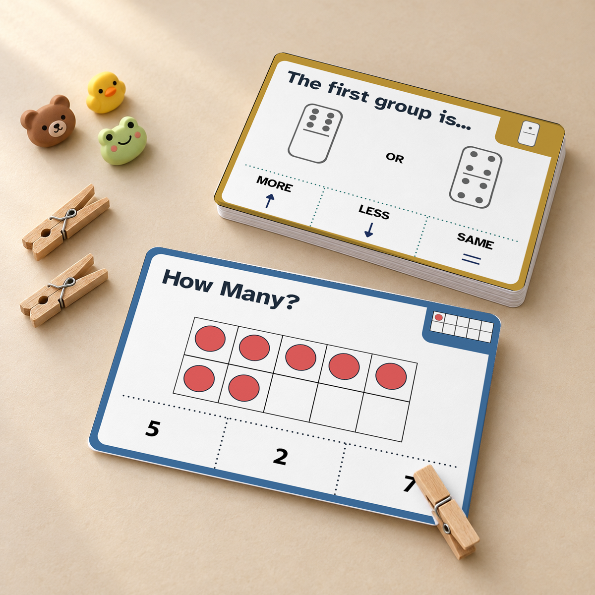 A children's math learning set on a beige surface, featuring printed cards with dominoes, tally marks, and number lines, plus small wooden clothespins and animal-shaped clips.